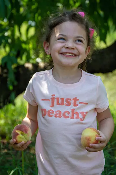 Little girl smiling with peach in her hand